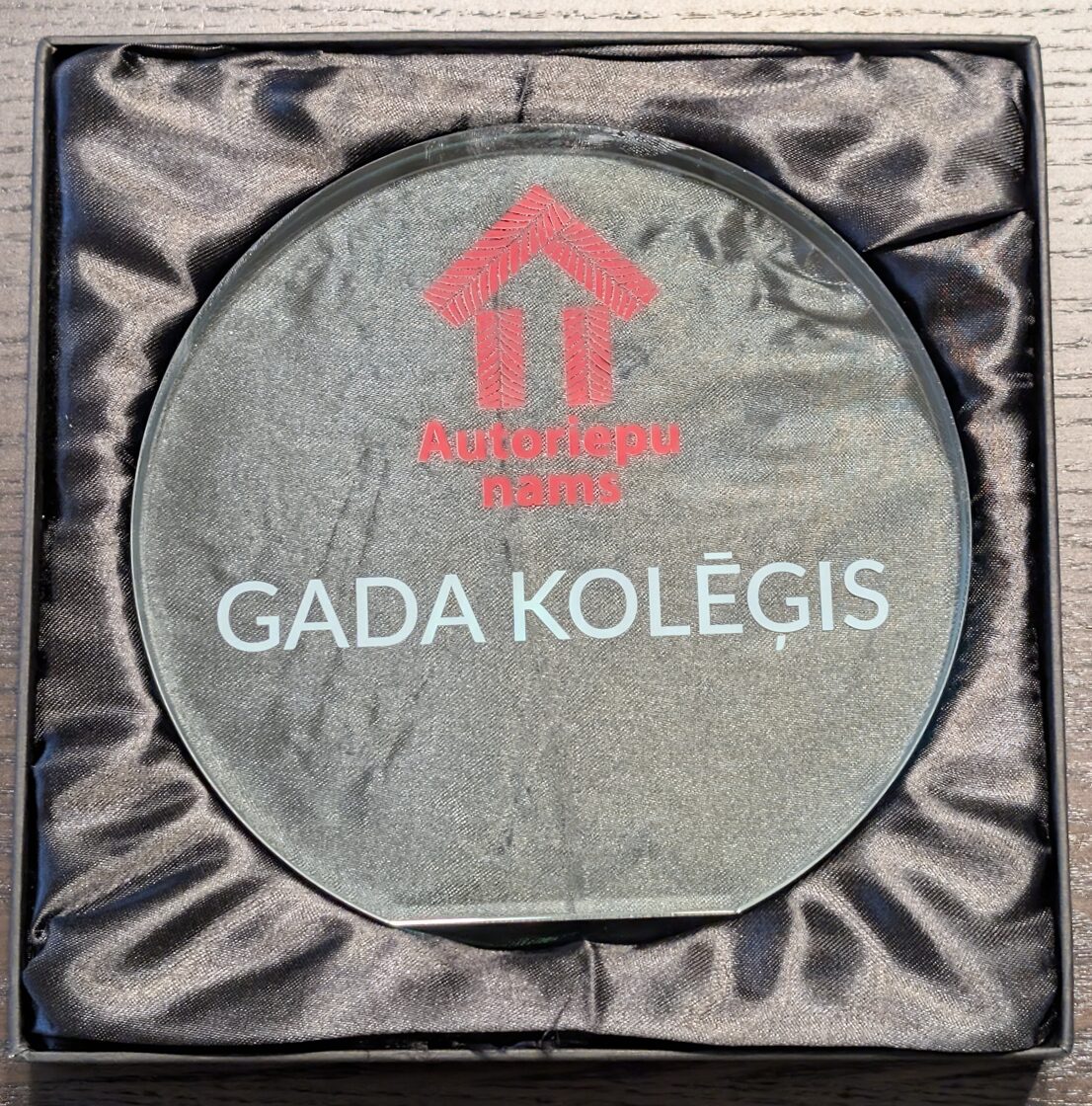 orporatīvā stikla balva Autoriepu nams ar sarkanu logo.